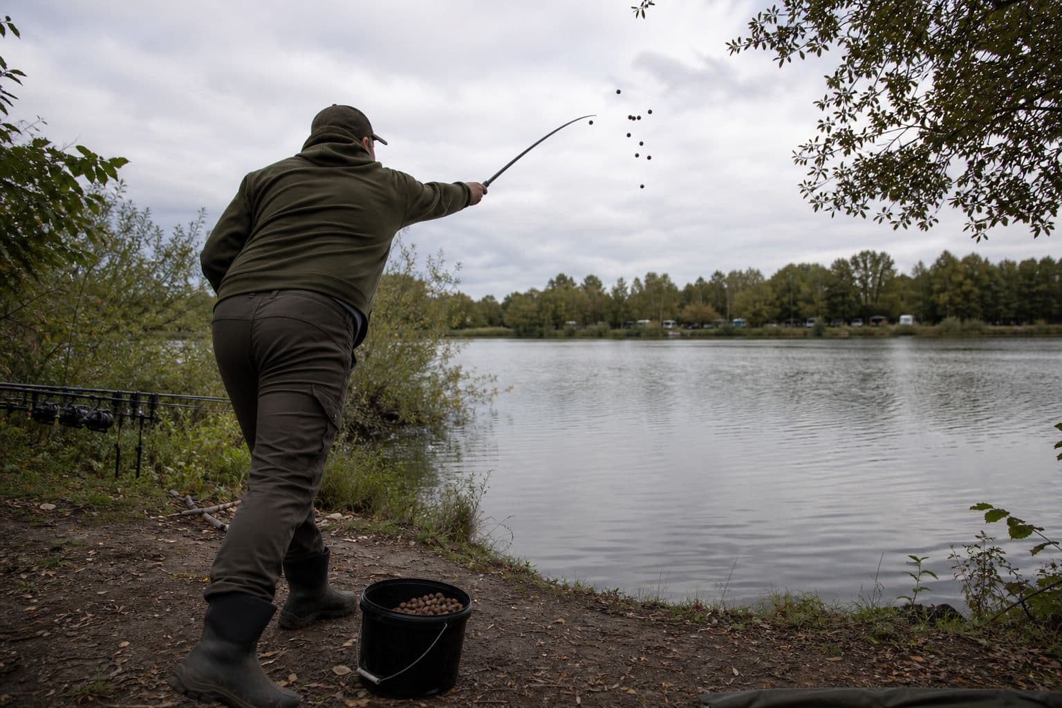 Boilies and pellet being introduced over a carp swim with a throwing stick